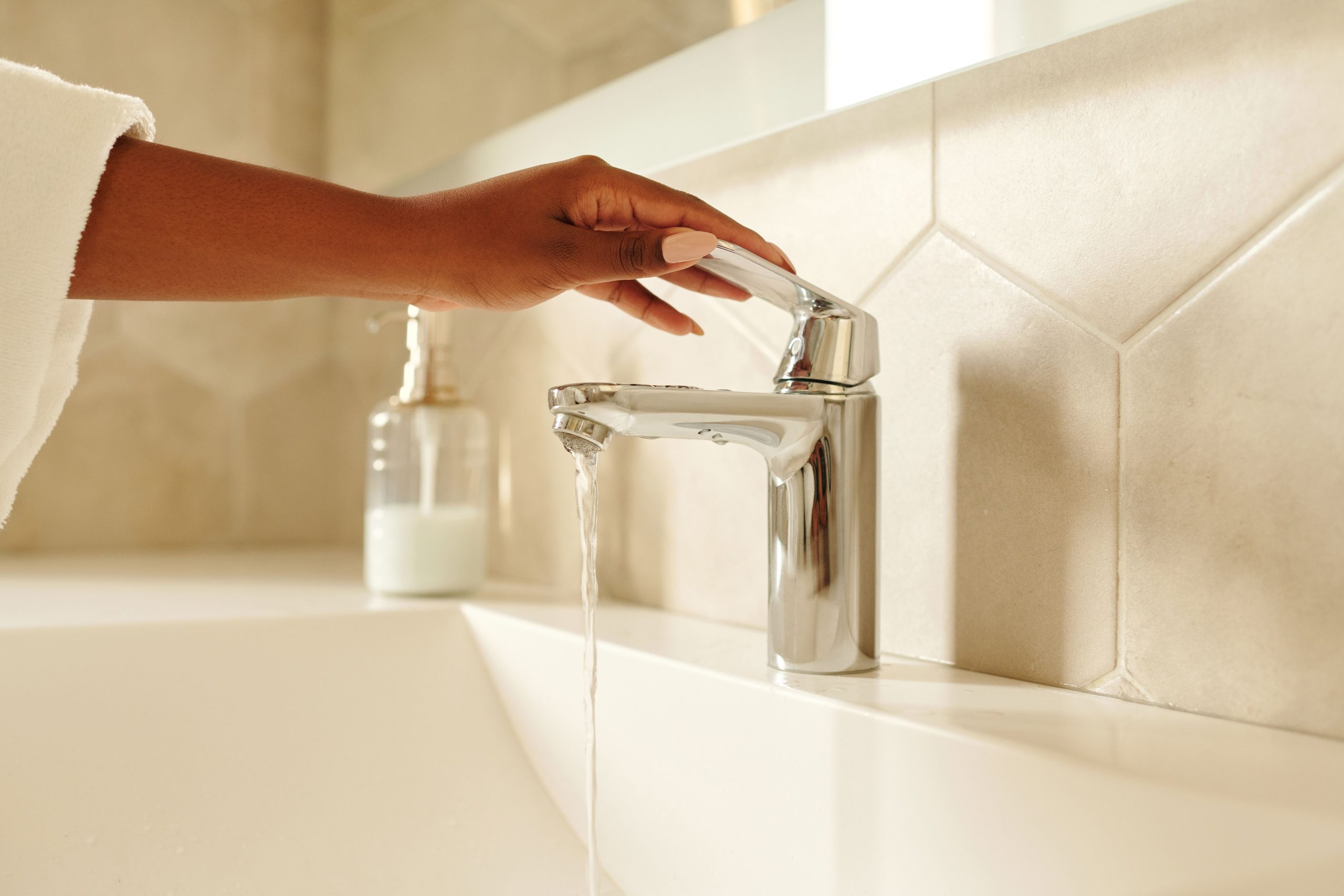 Main actionnant un robinet chromé avec eau