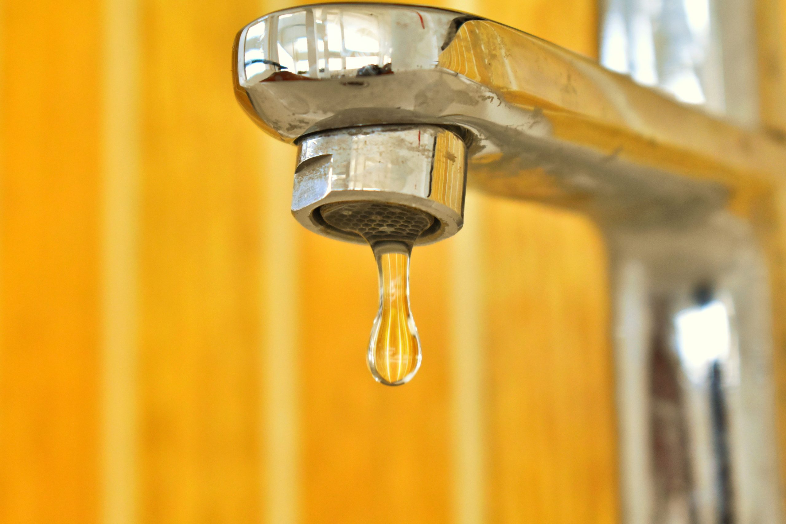 Goutte d'eau suspendue à un robinet inox